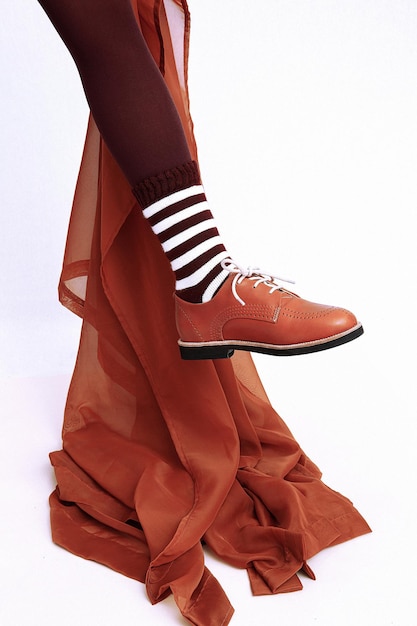 Onherkenbare vrouwenbenen die retro bruine klassieke schoenen, leggins en gestripte sokken dragen. Stijlvol textieldecor. Mode vintage minimalistisch winkelconcept