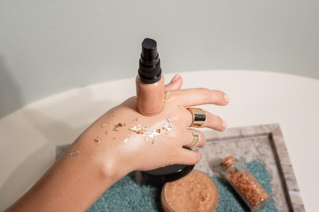 Onherkenbare vrouwenhand met gouden schittering klatergoud houdt kleurcrème vloeibare make-up foundationcrème boven cosmetica