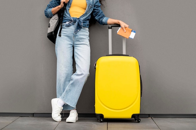 Foto onherkenbare vrouwenreiziger die zich over grijze achtergrond bevindt die gele bagage draagt