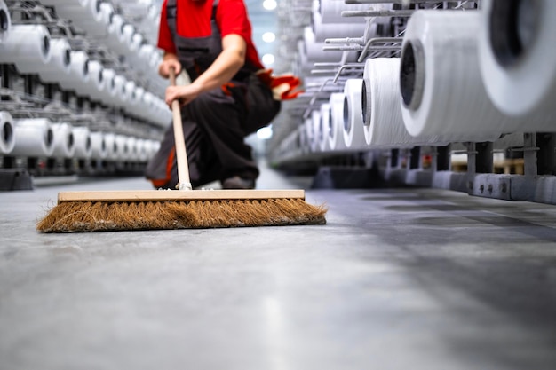 Onherkenbare werknemer die de vloer met een bezem schoonmaakt de fabriek netjes en schoon houdt