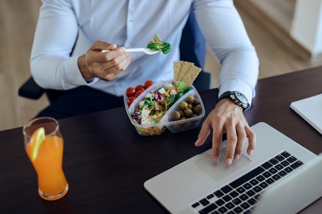 Onherkenbare zakenman die computer gebruikt terwijl hij een gezonde maaltijd op kantoor heeft