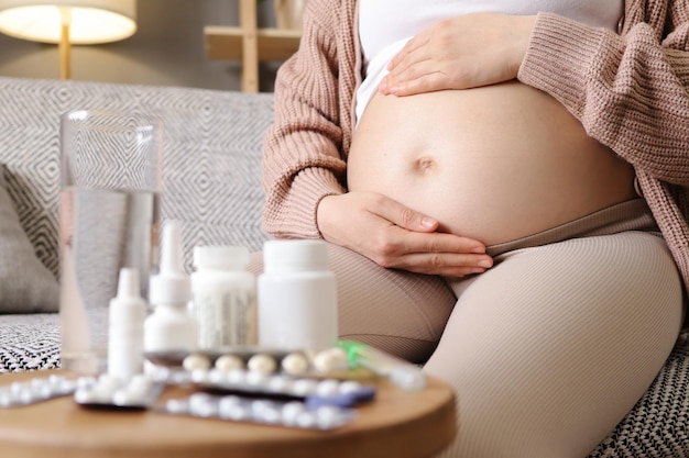 Foto onherkenbare zwangere vrouw die op de bank zit en haar ziekte behandelt toekomstige moeder die handen op haar buik houdt die gezondheidsproblemen heeft tijdens de zwangerschap