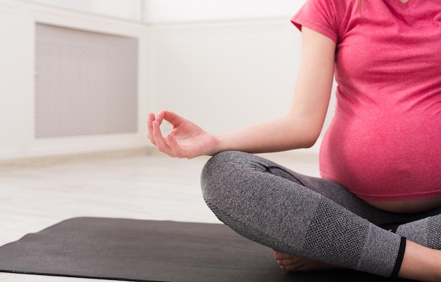 Onherkenbare zwangere vrouw die thuis mediteert, yoga beoefent. Rust, ontspanning, gezond zwangerschapsconcept, gewas, kopieerruimte
