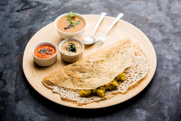 オニオンラヴァマサラドーサは、不機嫌そうな背景の上にチャツネとサンバーを添えた南インドのインスタント朝食です。セレクティブフォーカス