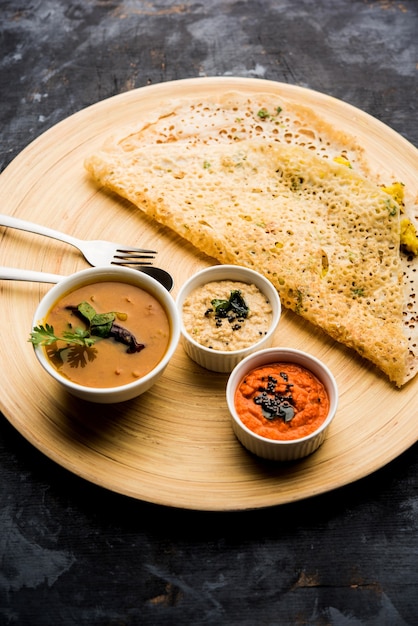 Onion rava masala dosa is a South Indian instant breakfast served with chutney and sambar over moody background. selective focus