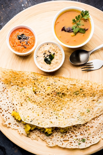 Photo onion rava masala dosa is a south indian instant breakfast served with chutney and sambar over moody background. selective focus