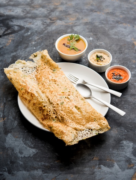 Photo onion rava masala dosa is a south indian instant breakfast served with chutney and sambar over moody background. selective focus