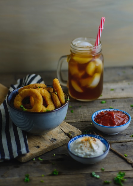 Onion rings, sauces and soda in a wood table