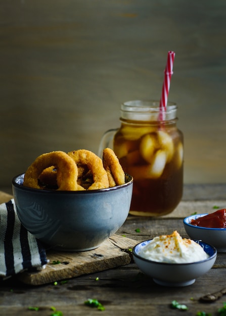 Onion rings, sauces and soda in a wood table