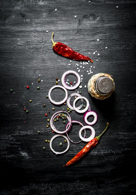 Onion rings and spices. On the black rustic background.