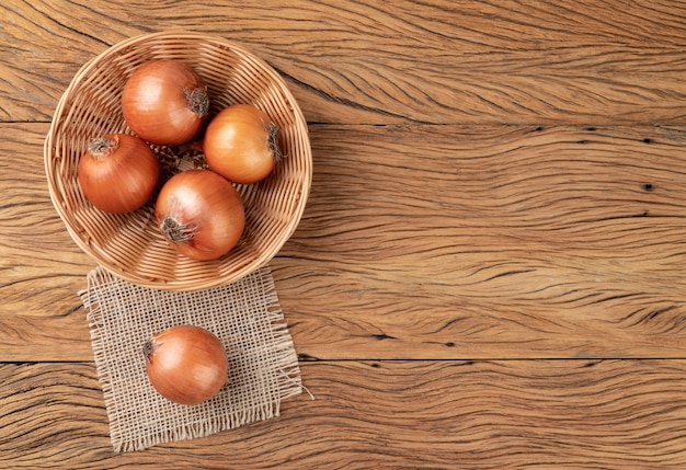 Onions in a basket over wooden table with copy space.