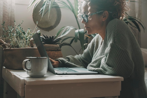 Online activiteit thuis met vrouw die laptop gebruikt zittend op de vloer op een tafeltje met groene tuinplanten op de achtergrond Internetverbinding Vrouwelijke mensen surfen op het web op zoek naar werk en info