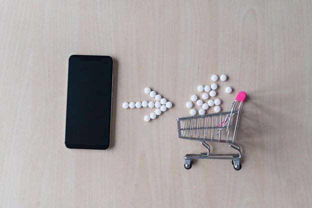 Online apotheekconcept Online medicijnen kopen via de telefoon Levering van geneesmiddelen Minitrolley met capsules en een smartphone met een zwart leeg scherm