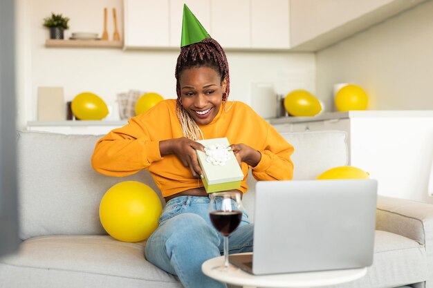 Online birthday party excited african american woman receiving gift from friends celebrating bday via video call