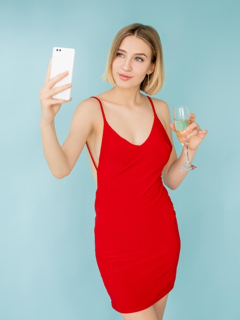 Online blog Streaming vrouw Feestviering Feestelijke stijl Mooie gelukkige dame rode jurk glas champagne op zoek smartphone geïsoleerd blauw