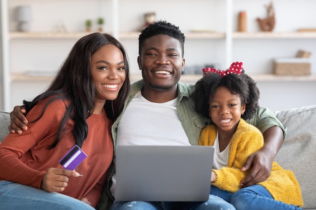 Online boekingen portret van gelukkige zwarte familie met laptop en creditcard