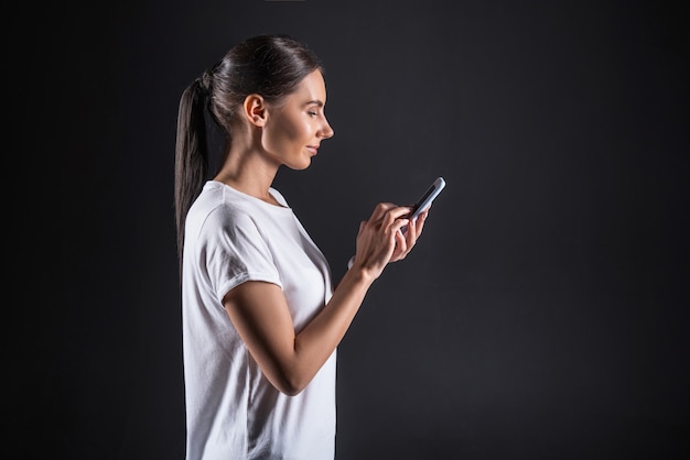 Online communication. Smart positive nice woman holding her smartphone and smiling while typing a message