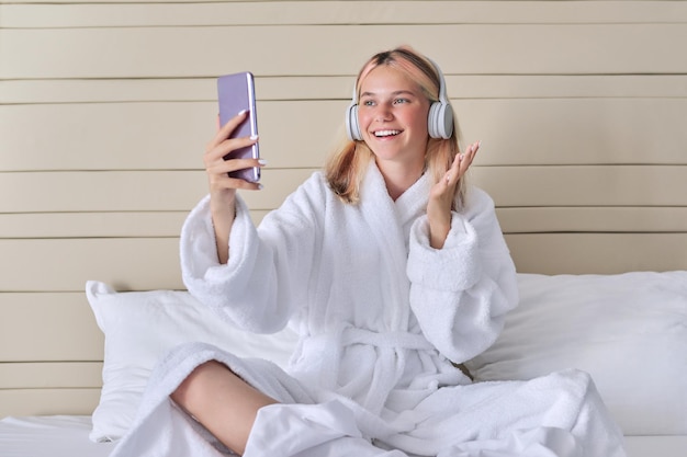 Online communication video call teenage girl in headphones with smartphone laughing and talking