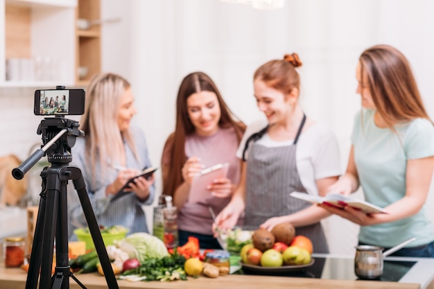 Online cooking classes. Food blogging. Group of women preparing meal and shooting video tutorial on mobile phone.