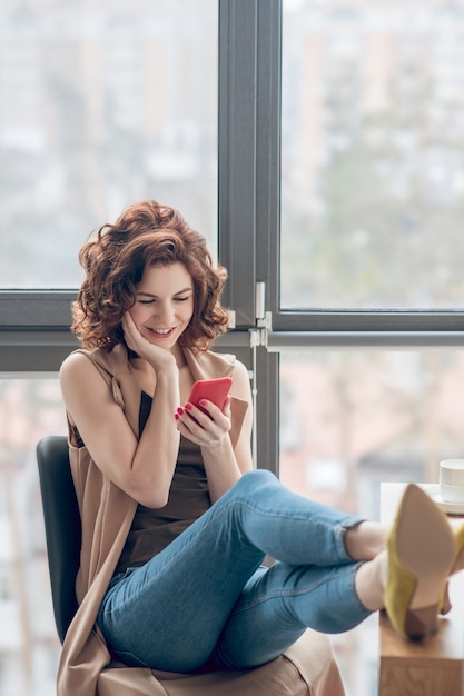 Online. Dark-haired woman sitting with telephone in hands