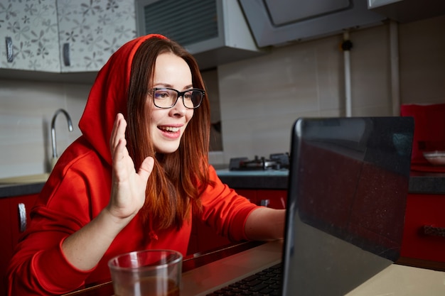 Online dating. Portrait of pleased red hair woman sitting in kitchen and making video call on laptop