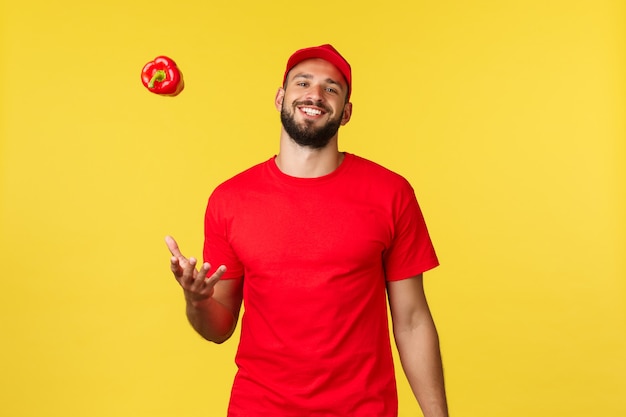 Online delivery shopping and food order concept carefree smiling courier in red uniform cap and tshi...