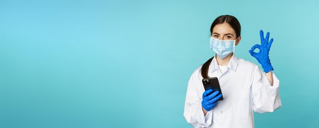 Online doctor and clinic young woman in medical face mask using\
smartphone for client remote online