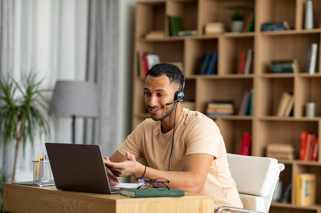 Online education arab male teacher having video chat with\
students using laptop and wearing wireless headphones