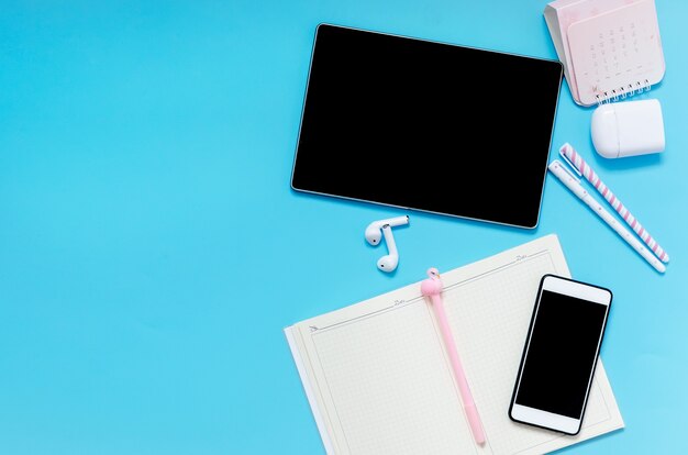 Online education concept. Tablet, phone, headphones, notebook, school supplies on blue background. Distance school in quarantine.