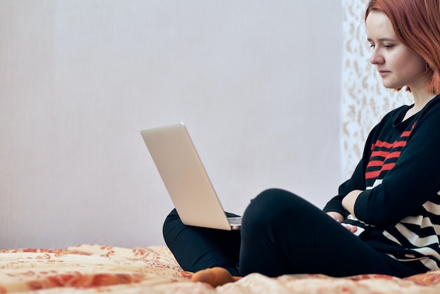 Online education. A girl in a striped jacket sits at home in quarantine and looks at the laptop. work home