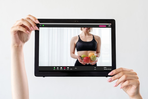オンラインフィットネスダイエット減量アプリ栄養ビデオチュートリアル光で隔離されたタブレット画面にフルーツボウルで認識できない運動女性を示す女性の手