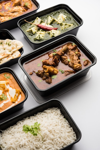 Online Food delivery concept Indian paneer butter masala and palak paneer, mutton &amp; chicken curry with roti and rice in plastic containers, food like butter chicken, chicken