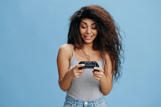 Online game ad concept enjoyed beautiful curly latin lady hold\
game pad near face ready to play cool rpg look at joystick gaming\
accessories brands ad studio shoot isolated blue background