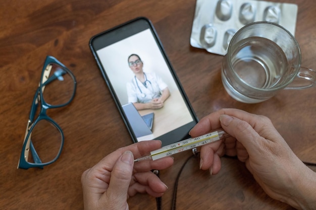 Online geneeskunde Een oude vrouw met symptomen van het coronavirus praat op een video met een viroloog Een gepensioneerde met koorts meet de temperatuur Telefonisch consult van de arts op afstand