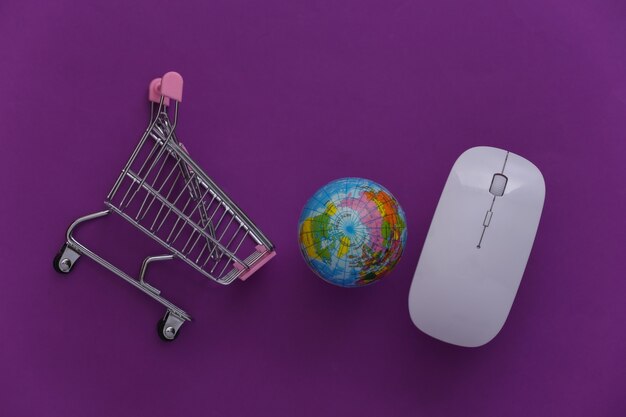 オンラインのグローバルスーパーマーケット。紫色の背景に地球儀とPCマウスとミニショッピングトロリー。上面図。フラットレイ