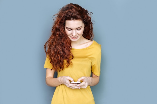 Online interactie. Vrolijke vrij aardige vrouw glimlachend en kijken naar haar smartphonescherm terwijl ze online met haar vrienden praat