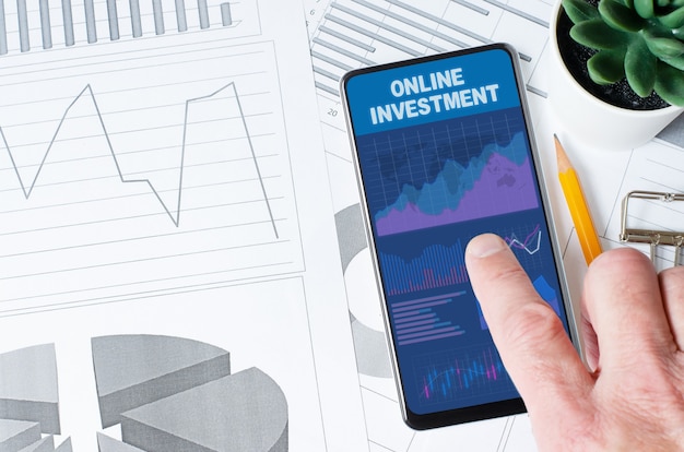 Online investment. A man is holding a smartphone with a mobile app with charts and graphs