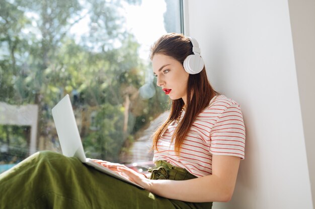 オンラインの仕事。コンピューターで働いている間ヘッドフォンを身に着けている深刻な女の子