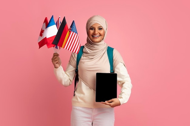 Online language courses muslim woman holding international flags and blank digital tablet