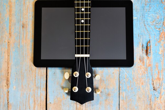 Online learning to play Hawaiian guitar. ukulele fretboard on wooden table next to tablet screen