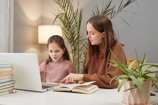 Online learning session Family webinar participation Remote schooling assistance Young mother and daughter using laptop in home interior doing homework together