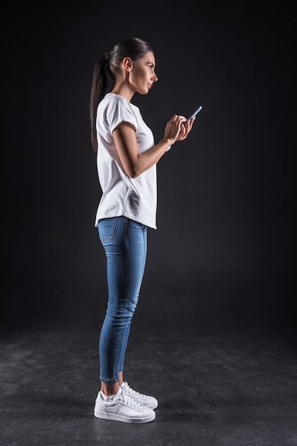 Online leeftijd. Vrolijke positieve aantrekkelijke vrouw staat en houdt haar smartphone vast tijdens het gebruik van sociale media