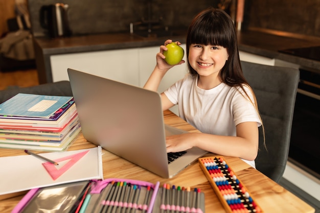 Online leren. Het schoolmeisje met groene appel doet thuiswerk