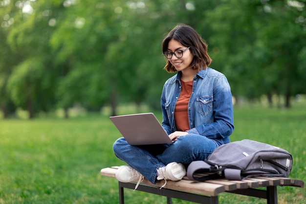 Online leren van jonge Arabische vrouw met Laptop zittend op een bankje In Park