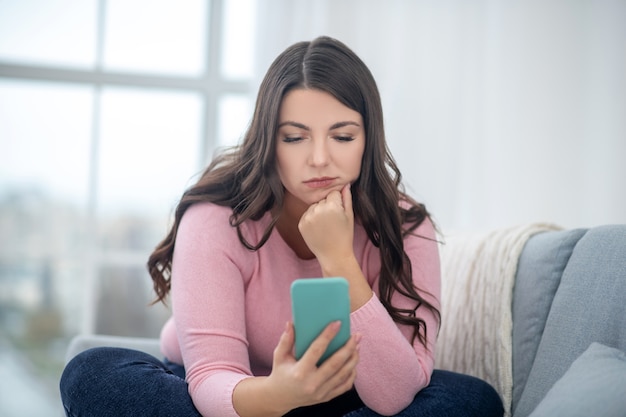 Online lezen. Volslanke jonge vrouw in een roze overhemd met een smartphone