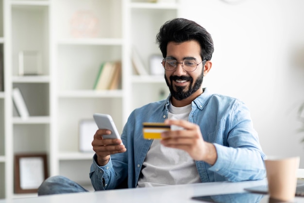 Online loan portrait of smiling indian man using smartphone and credit card