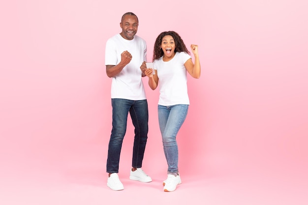 Online lottery Overjoyed black man and woman rejoicing success and holding smartphone exclaiming with triumph