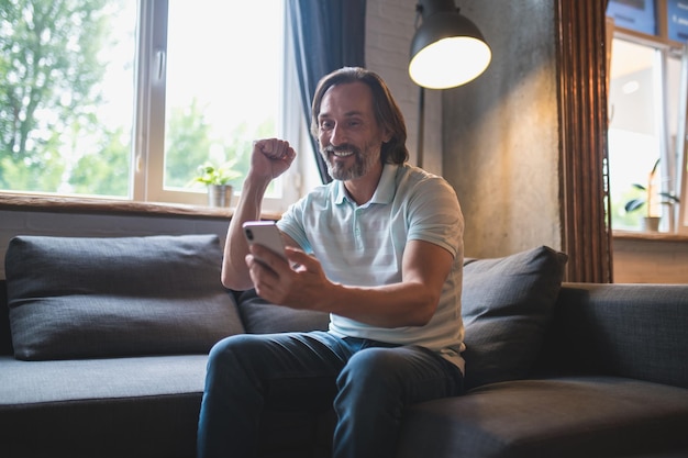 Online. Mature man spending time at home and watching something on his smartphone