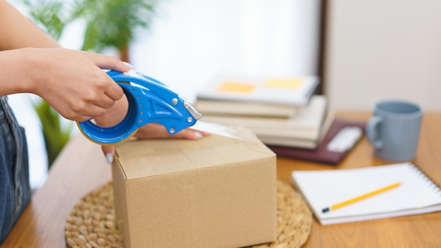 Online merchant concept Fashion designer packing clothes into parcel box and wrapping for delivery