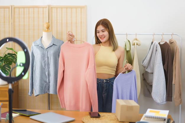 Online merchant concept Fashion designer showing clothes for sale in live streaming at home office